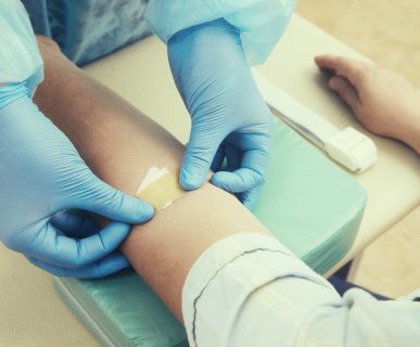 Pielęgniarka w sterylnym stroju nakleja pacjentowi plaster w miejscu, w którym uprzednio pobierała krew. /Źródło: 123rf.com