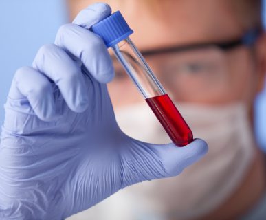 Analityk laboratoryjny w sterylnym ubraniu trzyma w dłoni fiolkę z krwią pacjenta. /Źródło: 123rf.com