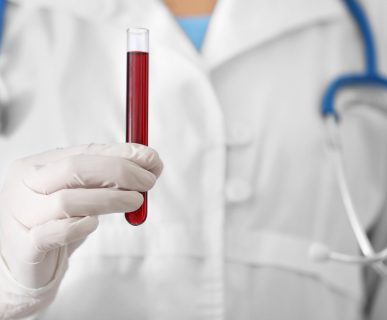 Pielęgniarz ubrany w biały strój medyczny, ze stetoskopem na szyi, trzyma w dłoni fiolkę wypełnioną krwią. /Źródło: 123rf.com