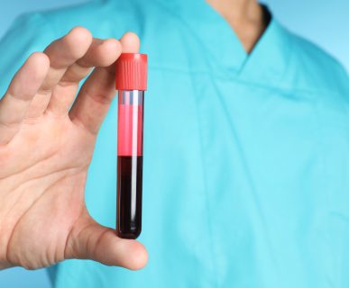 Pielęgniarz w sterylnym stroju medycznym trzyma w dłoni probówkę wypełnioną do połowy krwią pacjenta. /Źródło: 123rf.com