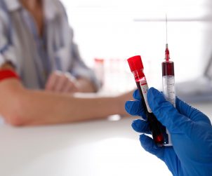 Pielęgniarka trzyma w dłoni odzianej w sterylną rękawiczkę, strzykawkę i probówkę wypełnione krwią pacjenta po pobraniu. /Źródło: 123rf.com