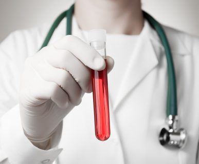 Lekarz ubrany w fartuch, ze stetoskopem na szyi, trzyma w dłoni probówkę wypełnioną krwią o jasnej barwie. /Źródło: 123rf.com