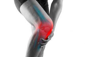 Mężczyzna, którego boli kolano, które jest wyraźniej zaznaczone na czerwono. /Źródło: 123rf.com