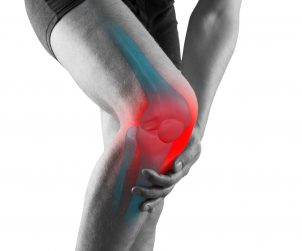 Mężczyzna, którego boli kolano, które jest wyraźniej zaznaczone na czerwono. /Źródło: 123rf.com
