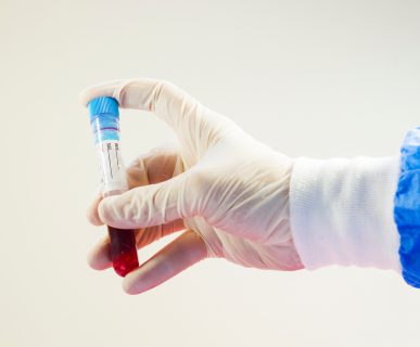 Analityk medyczny w sterylnym stroju trzyma w dłoni probówkę wypełnioną krwią. /Źródło: 123rf.com