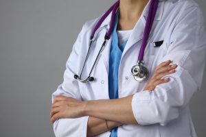 Lekarka ubrana w medyczny fartuch, z fioletowym stetoskopem na szyi stoi ze skrzyżowanymi rękoma. /Źródło: 123rf.com