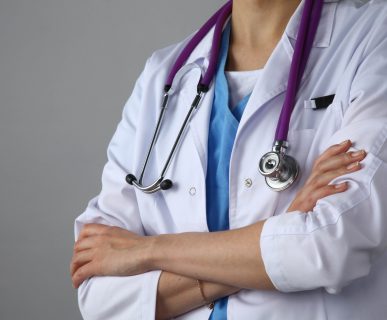 Lekarka ubrana w medyczny fartuch, z fioletowym stetoskopem na szyi stoi ze skrzyżowanymi rękoma. /Źródło: 123rf.com