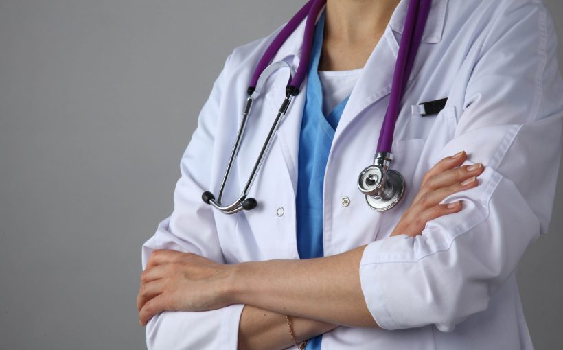 Lekarka ubrana w medyczny fartuch, z fioletowym stetoskopem na szyi stoi ze skrzyżowanymi rękoma. /Źródło: 123rf.com