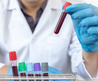 Pielęgniarz ubrany w strój medyczny trzyma w dłoni probówkę wypełnioną krwią pacjenta, aby odłożyć ją do specjalnego organizera. /Źródło: 123rf.com
