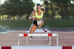 Młoda kobieta skacze przez płotki na torze lekkoatletycznym. /Źródło: 123rf.com