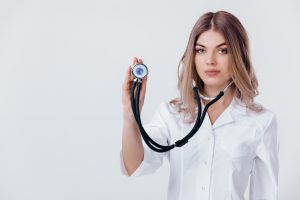 Młoda lekarka w fartuchu trzyma w dłoni stetoskop. /Źródło: 123rf.com