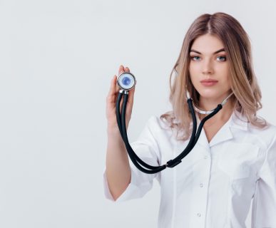Młoda lekarka w fartuchu trzyma w dłoni stetoskop. /Źródło: 123rf.com