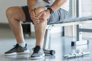 Mężczyzna trzyma się za bolące kolano po urazie podczas ćwiczeń na siłowni. /Źródło: 123rf.com