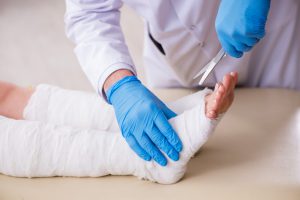 Lekarz ortopeda ściąga pacjentowi opatrunek na wizycie w przychodni. /Źródło: 123rf.com