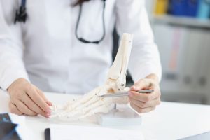 Lekarz wskazuje pacjentowi miejsce urazu na modelu układu kostnego stopy podczas konsultacji ortopedycznej. /Źródło: 123rf.com