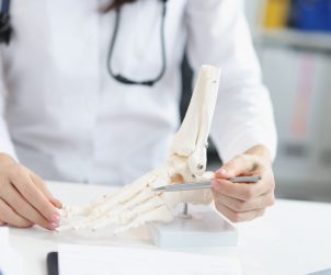 Lekarz wskazuje pacjentowi miejsce urazu na modelu układu kostnego stopy podczas konsultacji ortopedycznej. /Źródło: 123rf.com