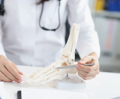 Lekarz wskazuje pacjentowi miejsce urazu na modelu układu kostnego stopy podczas konsultacji ortopedycznej. /Źródło: 123rf.com