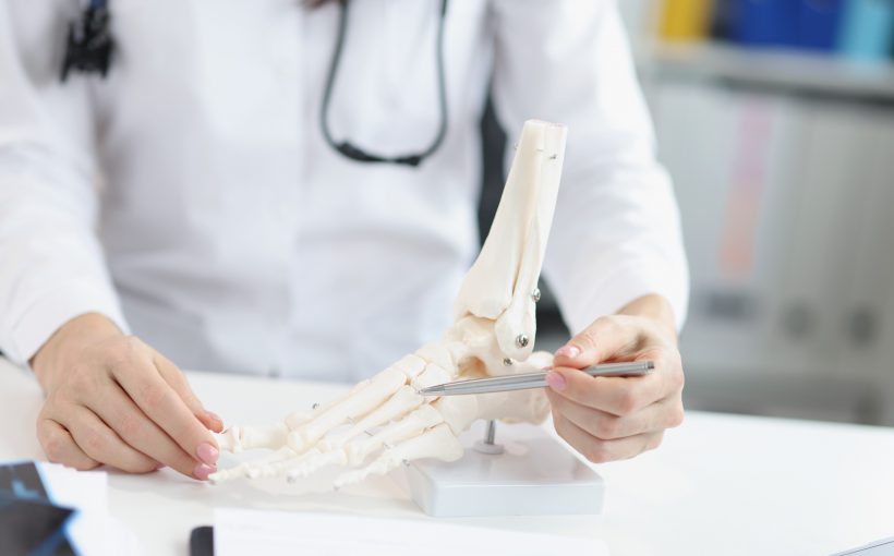 Lekarz wskazuje pacjentowi miejsce urazu na modelu układu kostnego stopy podczas konsultacji ortopedycznej. /Źródło: 123rf.com
