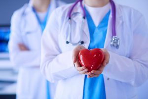 Lekarz kardiolog ubrany w medyczny strój trzyma w dłoni model serca. /Źródło: 123rf.com