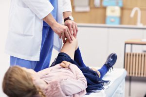 Lekarz ortopeda bada dziewczynce kolana po urazie. /Źródło: 123rf.com