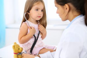 Mała pacjentka osłuchuje stetoskopem pluszowego misia, aby nie bać się podczas wizyty pediatrycznej. /Źródło: 123rf.com