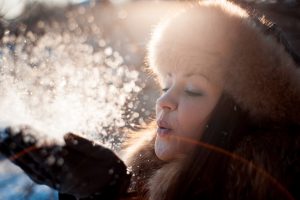 Kobieta w zimę zdmuchuje śnieg z rękawiczek. /Źródło: 123rf.com