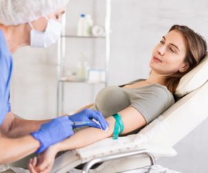 Pielęgniarka w sterylnym stroju pobiera młodej kobiecie krew z żyły u ręki. /Źródło: 123rf.com