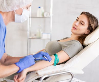 Pielęgniarka w sterylnym stroju pobiera młodej kobiecie krew z żyły u ręki. /Źródło: 123rf.com