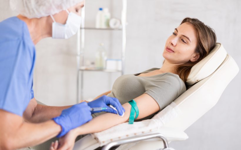 Pielęgniarka w sterylnym stroju pobiera młodej kobiecie krew z żyły u ręki. /Źródło: 123rf.com