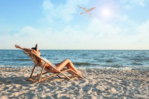 Młoda kobieta opala się na leżaku na plaży, w tle leci samolot. /Źródło: 123rf.com