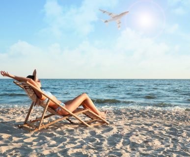 Młoda kobieta opala się na leżaku na plaży, w tle leci samolot. /Źródło: 123rf.com