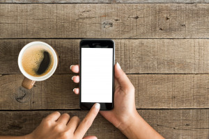 Kobieta korzysta z telefonu komórkowego, obok położony jest kubek z kawą. /Źródło: 123rf.com