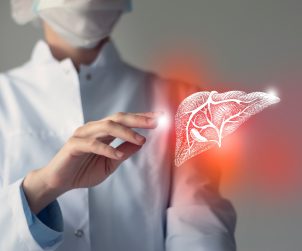 Lekarz ubrany w biały fartuch medyczny ma obok dłoni podświetloną grafikę wątroby. Źródło: 123rf.com