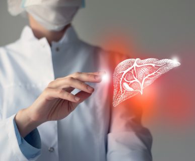 Lekarz ubrany w biały fartuch medyczny ma obok dłoni podświetloną grafikę wątroby. Źródło: 123rf.com