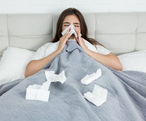 Kobieta leży chora w łóżku i wyciera nos w chusteczki. /Źródło: 123rf.com