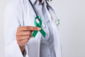 Lekarz trzyma w dłoni zieloną wstążkę na znak solidarności z osobami chorującymi na nowotwór. /Źródło: 123rf.com