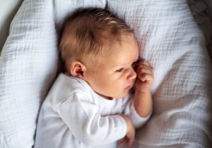 Niemowlę w białym ubranku leży w łóżku. /Źródło: 123rf.com