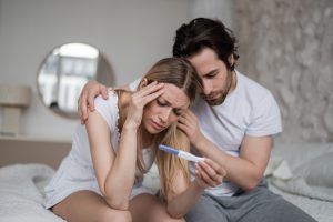 Mężczyzna i kobieta siedzą na łóżku, są smutni po zobaczeniu negatywnego wyniku testu ciążowego. Źródło: 123rf.com