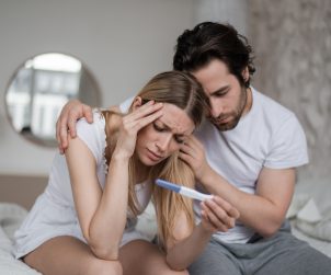 Mężczyzna i kobieta siedzą na łóżku, są smutni po zobaczeniu negatywnego wyniku testu ciążowego. Źródło: 123rf.com