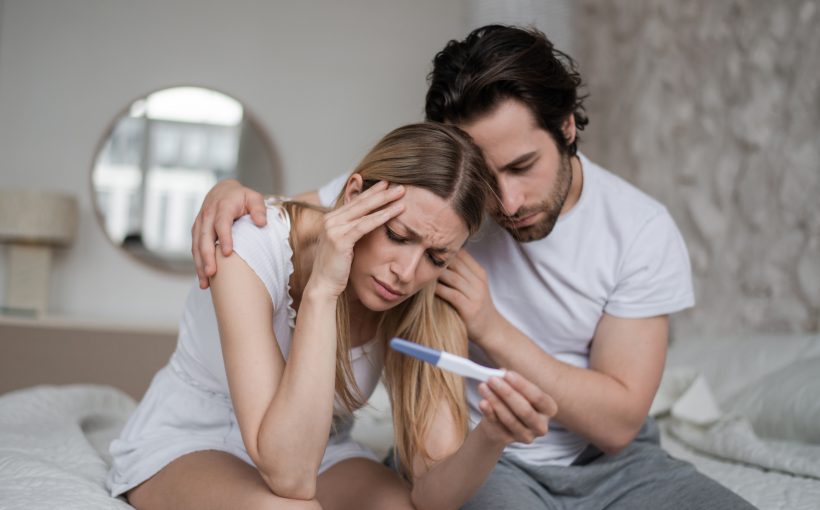Mężczyzna i kobieta siedzą na łóżku, są smutni po zobaczeniu negatywnego wyniku testu ciążowego. Źródło: 123rf.com