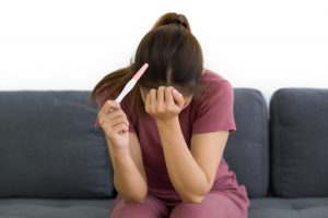 Smutna kobieta siedzi na łóżku, w dłoni trzyma negatywny test ciążowy. Źródło 123rf.com
