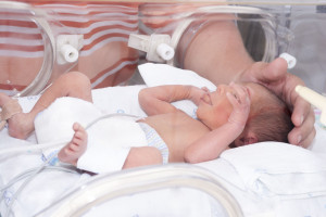 Noworodek leżący w inkubatorze, rodzic trzyma je za główkę. /Źródło: 123rf.com
