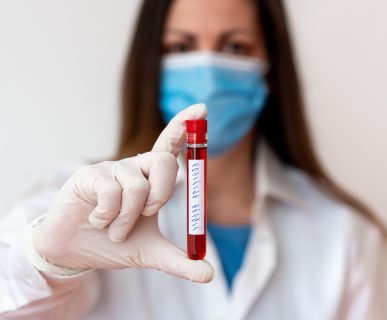 Pielęgniarka w sterylnym stroju trzyma w dłoniach fiolkę z próbką krwi pacjenta. Źródło: 123rf.com