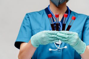 Lekarka ubrana w stój medyczny ze stetoskopem na szyi trzyma w dłoniach pobrane wcześniej fiolki z próbką krwi pacjenta.