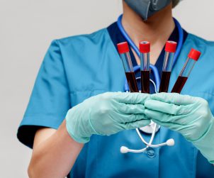 Lekarka ubrana w stój medyczny ze stetoskopem na szyi trzyma w dłoniach pobrane wcześniej fiolki z próbką krwi pacjenta. Źródło: 123rf.com