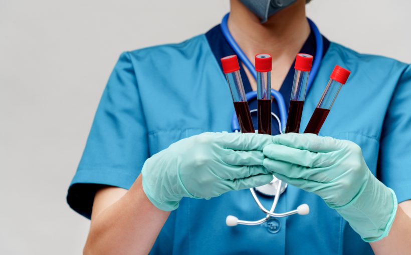 Lekarka ubrana w stój medyczny ze stetoskopem na szyi trzyma w dłoniach pobrane wcześniej fiolki z próbką krwi pacjenta. Źródło: 123rf.com