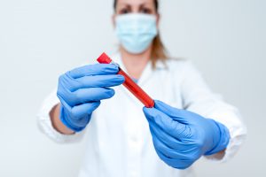 Pielęgniarka trzyma w dłoniach odzianych w sterylne rękawiczki fiolkę z próbką krwi pacjenta do analizy laboratoryjnej. Źródło: 123rf.com