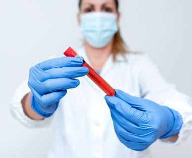 Pielęgniarka trzyma w dłoniach odzianych w sterylne rękawiczki fiolkę z próbką krwi pacjenta do analizy laboratoryjnej. Źródło: 123rf.com