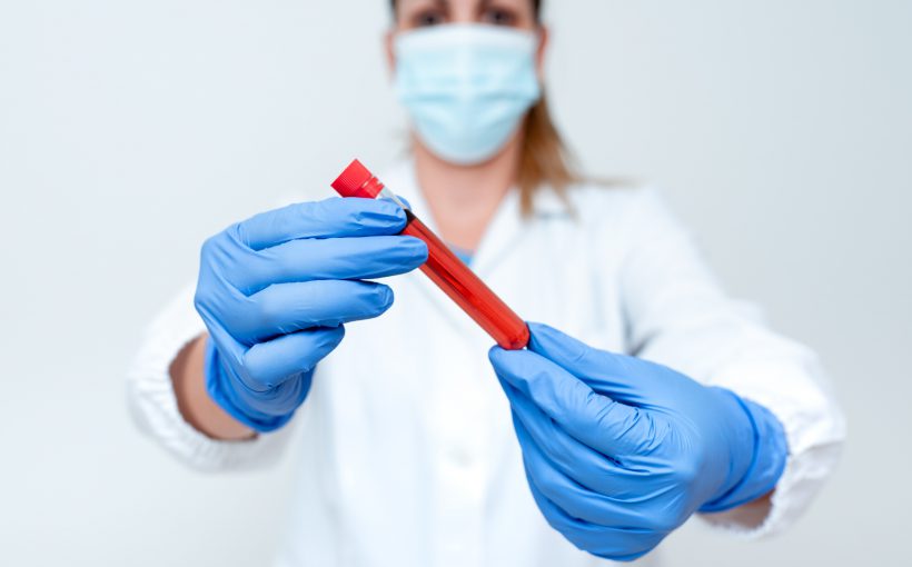 Pielęgniarka trzyma w dłoniach odzianych w sterylne rękawiczki fiolkę z próbką krwi pacjenta do analizy laboratoryjnej. Źródło: 123rf.com