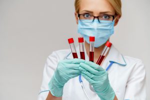 Pielęgniarka trzyma w dłoniach cztery fiolki z krwią pobraną do analizy laboratoryjnej w celu diagnostyki.